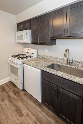 Kitchen with white appliances and dark wood cabinets at McDonogh Village Apartments & Townhomes, Randallstown, Maryland